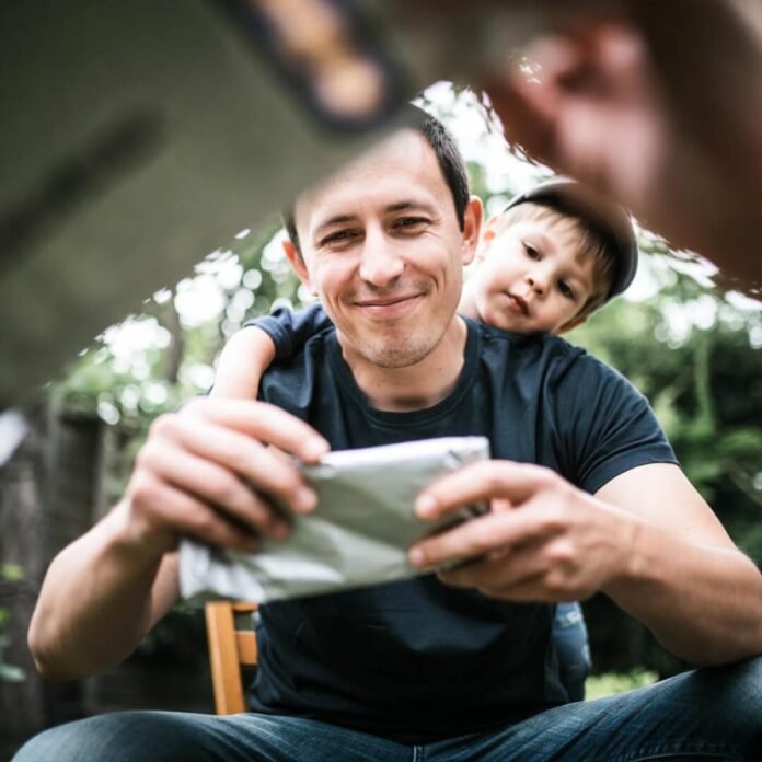 Dad unwraps gift with kid peeking.